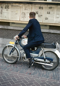 849505 Afbeelding van een man op een bromfiets die de krant leest in de vitrines van het kantoor van het Utrechts ...